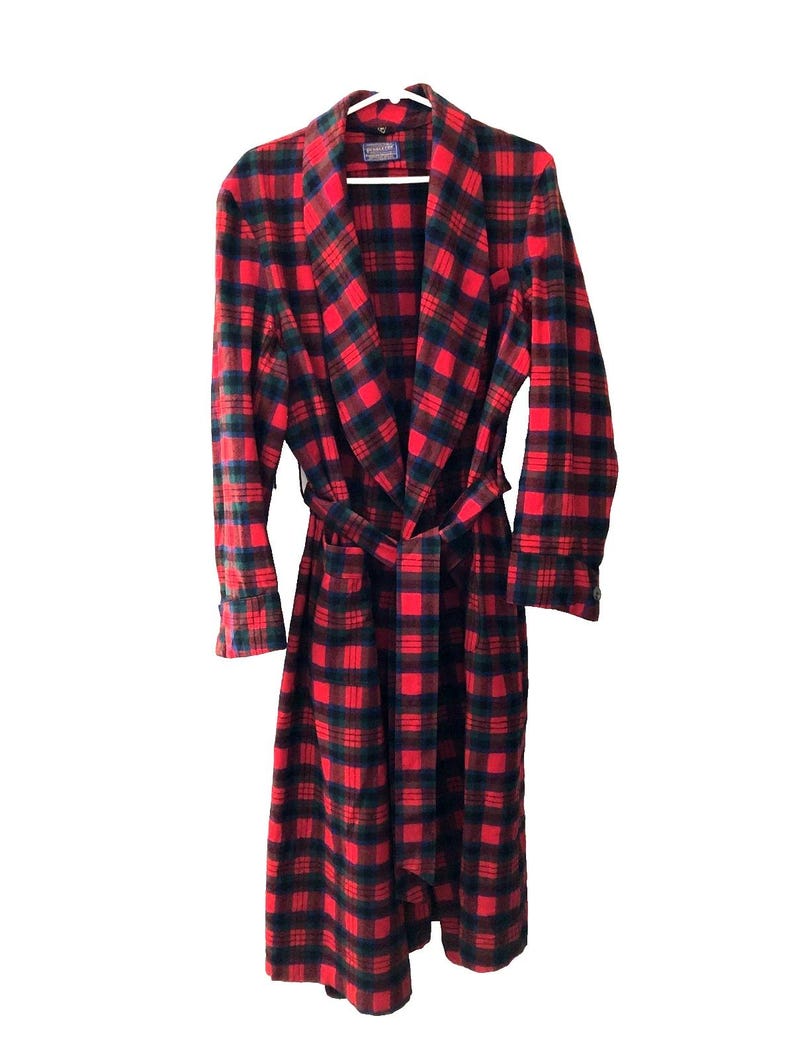 May include: A long-sleeved robe featuring a red and dark green plaid pattern. The garment includes a shawl collar, a matching fabric tie belt at the waist, and a Pendleton brand label visible at the inner neckline. The robe hangs on a white hanger.