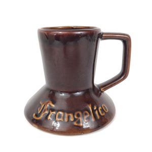 May include: A brown ceramic mug with a handle, featuring the word "Frangelico" in a lighter brown script. The mug has a unique shape, wider at the base and tapering towards the top.