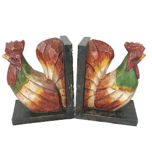 May include: A pair of hand-carved wooden bookends featuring rooster designs. The roosters are painted with red, green, yellow, and white hues. The bookends have a black base and are ideal for holding books on a shelf or desk.