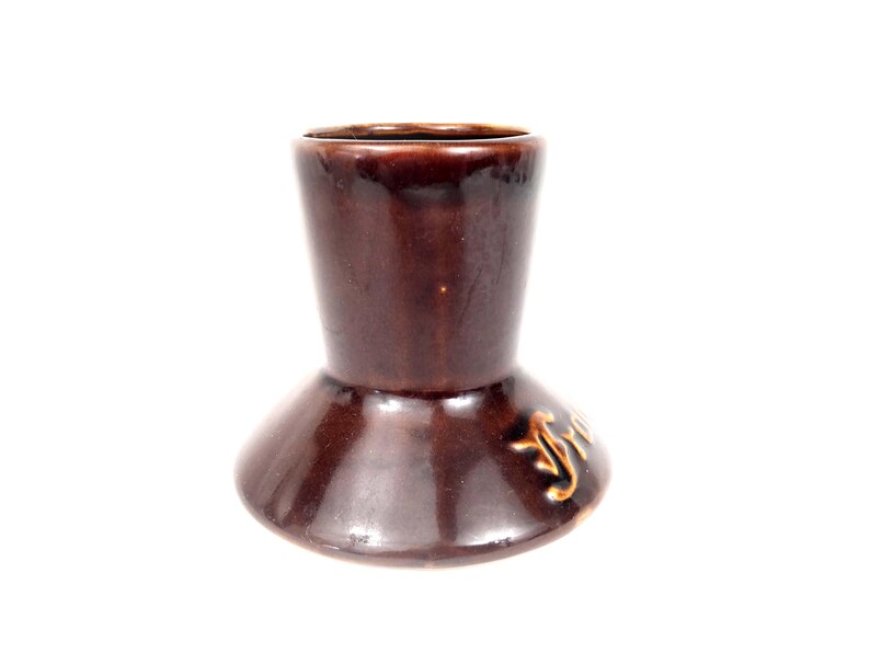 May include: A brown ceramic candlestick holder with a flared base and a narrower top. The candlestick holder has a glossy finish and a decorative design on the side.