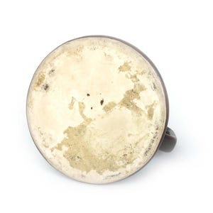 May include: A brown ceramic mug, seen from below, with a handle. The base interior is off-white with brown and tan staining. The mug is set against a white background.