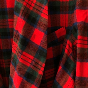 May include: A blazer featuring a vibrant red, dark green, and navy blue plaid tartan pattern. The garment has a structured lapel, long sleeves, and a single visible welt pocket on the front panel, showcasing a classic woven textile construction.