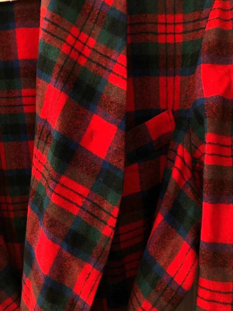 May include: A blazer featuring a vibrant red, dark green, and navy blue plaid tartan pattern. The garment has a structured lapel, long sleeves, and a single visible welt pocket on the front panel, showcasing a classic woven textile construction.