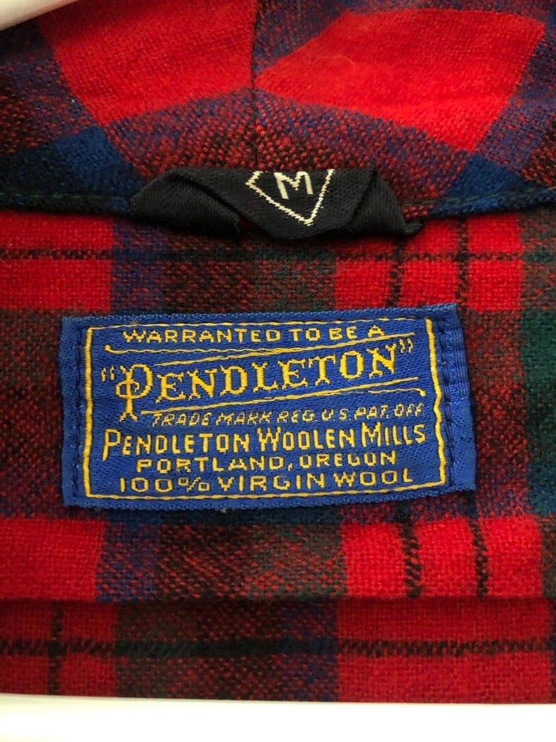 May include: A red and blue plaid shirt featuring a black size M tag and a blue rectangular label with yellow text reading Warranted to be a Pendleton, Pendleton Woolen Mills, Portland, Oregon, 100% Virgin Wool, Trade Mark Reg. U.S. Pat. Off.