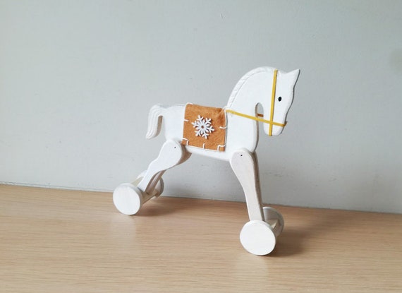 Christmas horse on wheels, white rocking horse retro toy, white horse with brown blanket saddle and a snowflake, decorative Xmas horse