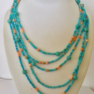 May include: Multi-strand turquoise and coral bead necklace. The necklace features five strands of turquoise beads, interspersed with larger turquoise beads and smaller coral beads. The necklace is accented with gold beads.