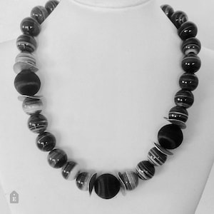 May include: A black and white striped beaded necklace with a large black bead in the center.