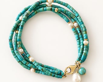 Può includere: Un bracciale a più fili composto da piccole perline cilindriche di turchese alternate a perle bianche e minuscoli distanziatori in metallo dorato. Il bracciale è chiuso da un moschettone dorato, da cui pendono una perla e una perlina turchese.