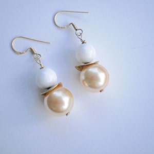 May include: A pair of gold tone earrings with two white and two cream colored round beads.