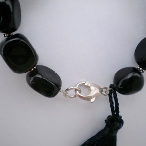 Pu&ograve; includere: Un bracciale con perline nere lisce e lucide, separate da piccoli distanziatori in metallo color argento. Il gioiello &egrave; fissato con una chiusura a moschettone color argento e presenta una nappa in filo nero vicino alla chiusura.