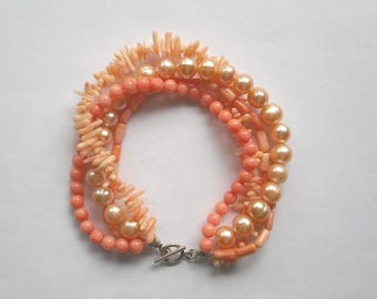 Può includere: Bracciale a più fili con perline e perle color corallo e pesca. Il bracciale ha una chiusura color argento. I pezzi di corallo hanno un aspetto strutturato, simile a un ramo, che aggiunge un elemento unico al gioiello.
