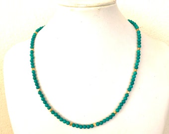 May include: A beaded necklace featuring small, round, turquoise-colored beads interspersed with tiny, metallic gold-toned spacer beads. The necklace is arranged in a circular shape, showcasing a consistent pattern of blue beads separated by gold accents.