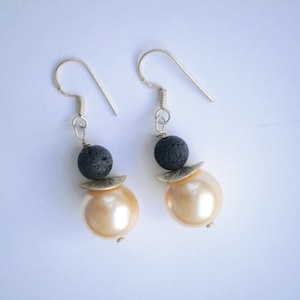 May include: A pair of earrings with a black lava rock bead and a large, cream-colored pearl bead.