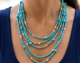 May include: A multi-strand necklace featuring turquoise blue seed beads interspersed with round and cylindrical peach-colored beads and small metallic gold spacers. The layered design creates a cascading effect around the neck area.