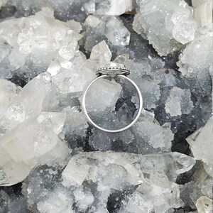 K&ouml;nnte beinhalten: Ein silberner Ring mit einem klaren Edelstein, der in einer Zargenfassung gefasst ist. Der Ring ist von kleinen silbernen Perlen umgeben.