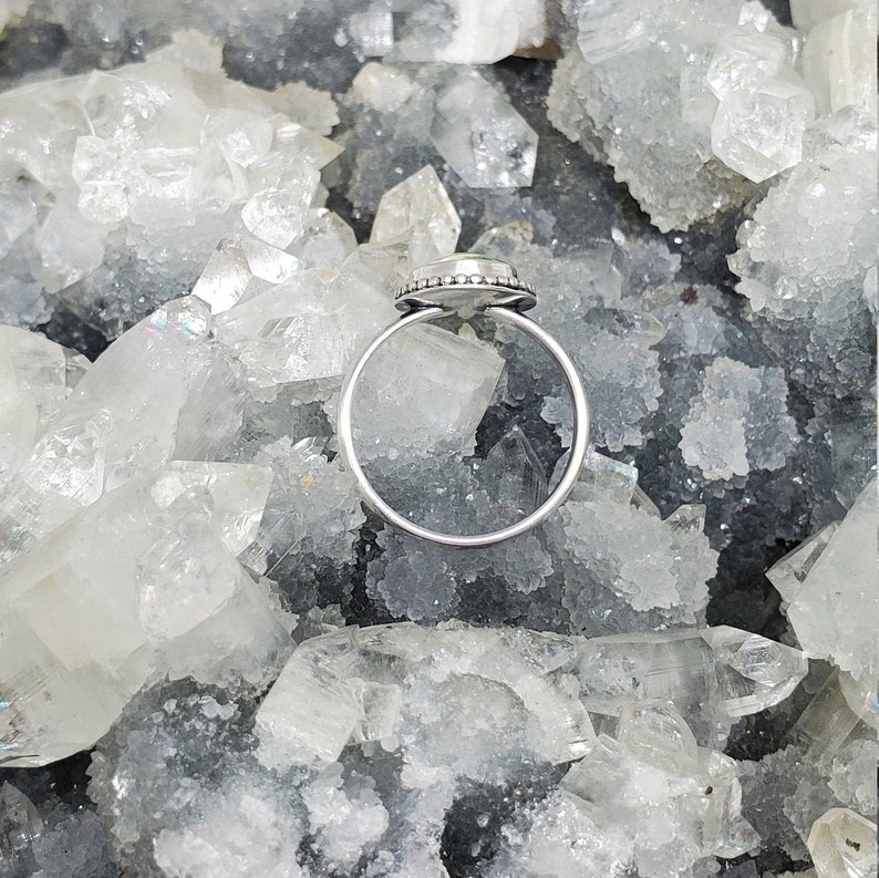 K&ouml;nnte beinhalten: Ein silberner Ring mit einem klaren Edelstein, der in einer Zargenfassung gefasst ist. Der Ring ist von kleinen silbernen Perlen umgeben.