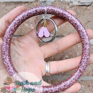 May include: A pink glitter key ring with a small pink heart charm attached. The key ring is made of a thick, durable material and is perfect for holding keys, ID badges, or other small items.