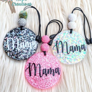 May include: Three round car air fresheners with the word "Mama" written on them. The air fresheners are made of clear resin with glitter and come in black, white, and pink.