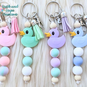 May include: Four colorful rubber ducky keychains with beaded strands. The ducks are pink, green, purple, and blue. Each keychain has a silver key ring with a tassel.
