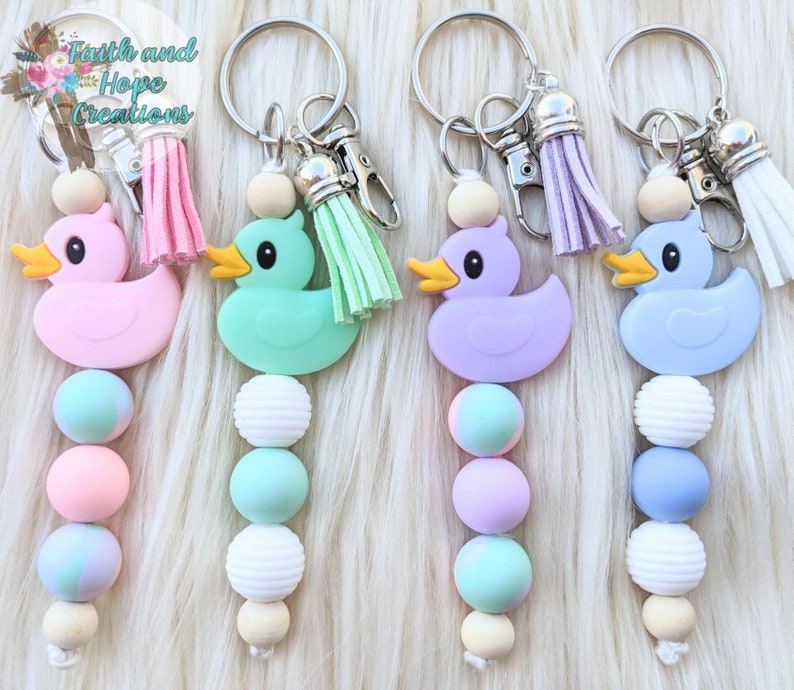 May include: Four colorful rubber ducky keychains with beaded strands. The ducks are pink, green, purple, and blue. Each keychain has a silver key ring with a tassel.