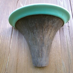 May include: A wall-mounted planter made of wood with a light blue ceramic rim. The planter has a ribbed texture and a funnel shape.