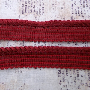 May include: Two pieces of red braided trim with a textured woven design. The trim is approximately 1 inch wide.