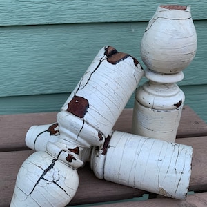 May include: Three white painted wooden finials with distressed paint and brown wood showing through. The finials are stacked on top of each other.