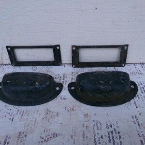May include: Two sets of black metal drawer pulls. Each pull has a rectangular plate with a cutout for a handle. The handles are rounded and have a slightly textured surface.
