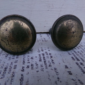 May include: Two antique brass cabinet knobs with a worn, aged finish. The knobs have a round shape with a raised edge.