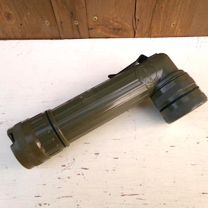 May include: An olive drab, right-angle flashlight with a ribbed body and a black strap. The flashlight has a cylindrical design with a rotating head and a textured grip. The brand name is visible on the side.