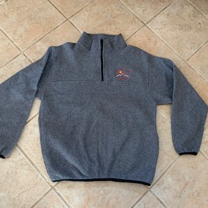 May include: A gray fleece pullover with a black zipper and black trim. The pullover has an embroidered logo on the left chest that says "Mountain High Country".