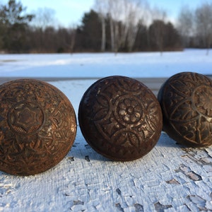 May include: Three antique door knobs with intricate, ornate designs. The knobs are made of dark brown metal and have a worn, rustic look.