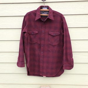 May include: A burgundy flannel shirt with a button-down collar and two chest pockets. The shirt has a faded, distressed look.