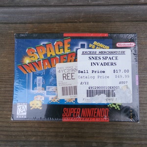 May include: A Super Nintendo game cartridge for Space Invaders, featuring a pixelated image of the game on the front. The game is priced at $17.00 and $49.99.
