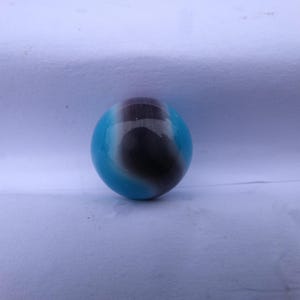 May include: A spherical glass marble featuring a smooth, polished surface with a distinct color pattern. The design consists of a deep, dark brown central band that transitions into vibrant, bright blue sections on both sides of the sphere.