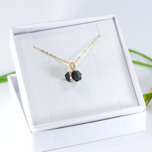 May include: A gold chain necklace with a black raw crystal pendant. The crystal is wrapped in gold wire.