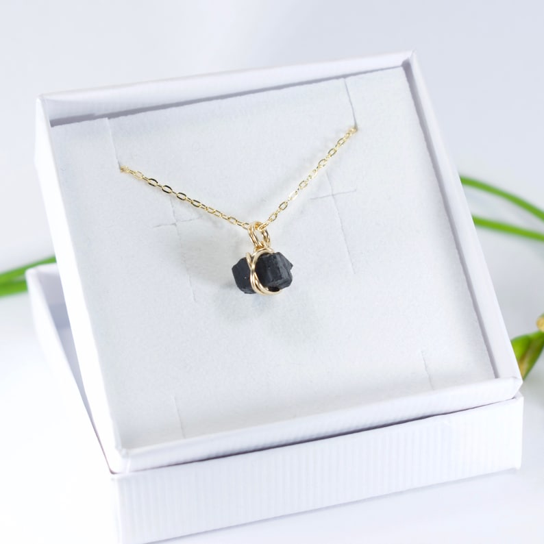 May include: A gold chain necklace with a black raw crystal pendant. The crystal is wrapped in gold wire.
