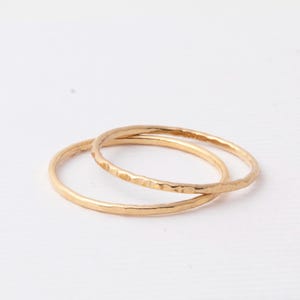 Könnte beinhalten: Zwei goldfarbene Ringe vor weißem Hintergrund. Ein Ring hat eine gehämmerten Textur, der andere ist glatt. Die Ringe sind kreisförmig und scheinen aus Metall zu sein.