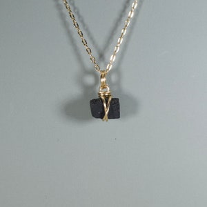 May include: A black stone pendant wrapped in gold wire, hanging from a gold chain necklace.