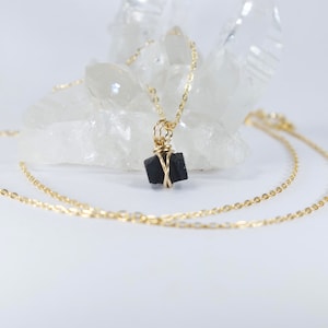 May include: A gold chain necklace with a black stone pendant wrapped in gold wire. The necklace is displayed on a white crystal.