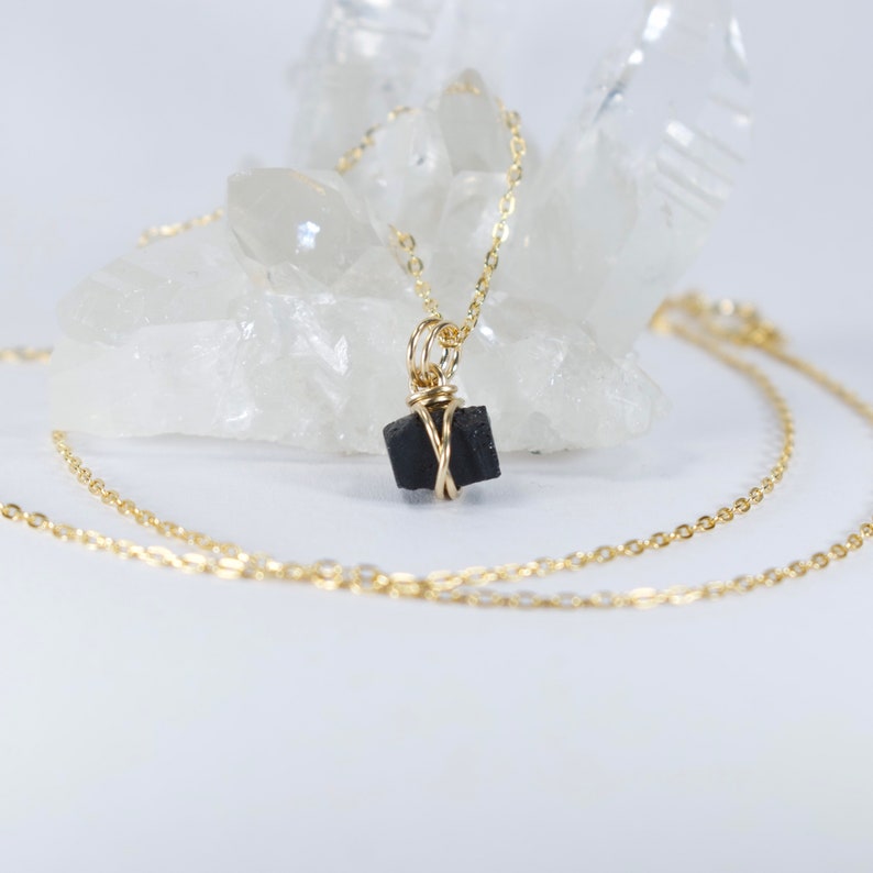 May include: A gold chain necklace with a black stone pendant wrapped in gold wire. The necklace is displayed on a white crystal.