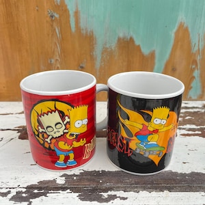 May include: Two ceramic mugs with a red and black background featuring a cartoon character skateboarding with flames. The text "Bart" and "Beast" are visible on the mugs.
