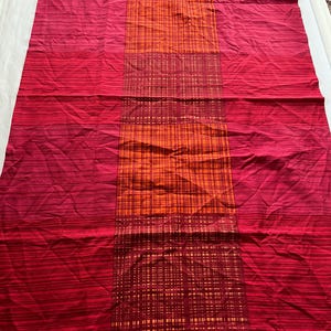 Könnte beinhalten: Ein roter und orangefarbener Stoff mit einem gestreiften und karierten Muster. Der Stoff hat einen Farbverlauf, der von tiefem Rot zu einem helleren Farbton übergeht, mit einem orangefarbenen Karoteil in der Mitte. Der Stoff wird wahrscheinlich für die Inneneinrichtung verwendet.