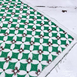 Peut inclure: Un tissu blanc avec un motif géométrique vert et marron. Le tissu a une bordure blanche et est plié sur lui-même.