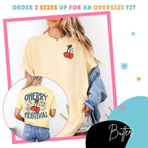 K&ouml;nnte beinhalten: Ein hellgelbes T-Shirt mit einem Kirsch-Motiv auf der Vorder- und R&uuml;ckseite. Auf der R&uuml;ckseite des Shirts steht "Cherry Festival" mit einem Kirsch- und G&auml;nsebl&uuml;mchen-Design. Der Text "Order 2 sizes up for an oversize fit" steht oben.