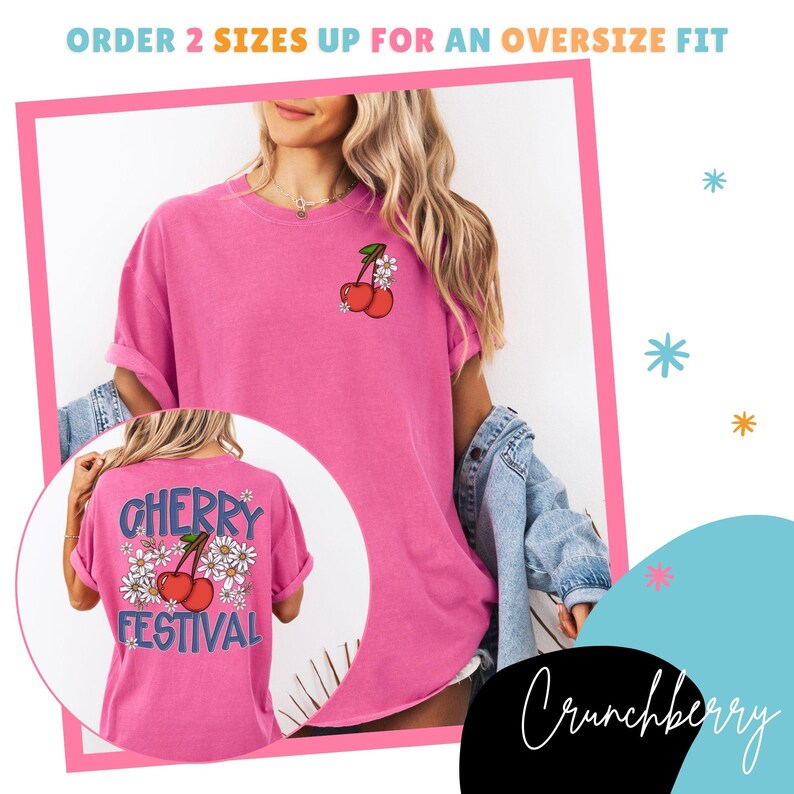 K&ouml;nnte beinhalten: Ein pinkfarbenes T-Shirt mit einem Kirsch- und G&auml;nsebl&uuml;mchen-Motiv. Auf der R&uuml;ckseite des Shirts steht "CHERRY FESTIVAL" in blauer Schrift. Das Shirt hat hochgekrempelte &Auml;rmel und eine lockere Passform.