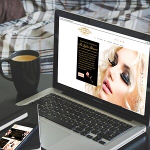 May include: A laptop computer displaying a website for a beauty salon called "Beauty in the Eye". The website features a black and white photo of a woman with long eyelashes and the text "The Perfect Enhancement".