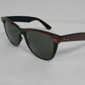 May include: Black and brown Ray-Ban sunglasses with green lenses. The sunglasses have a textured brown frame and a black frame.