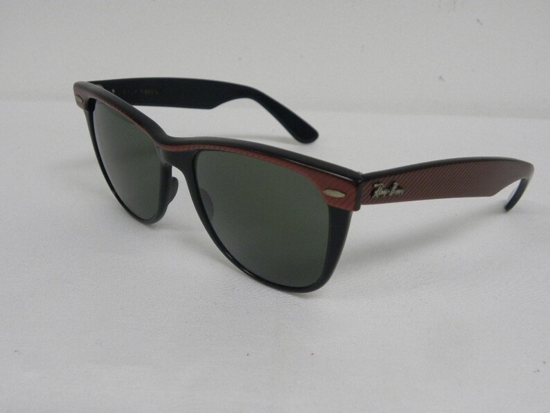 May include: Black and brown Ray-Ban sunglasses with green lenses. The sunglasses have a textured brown frame and a black frame.