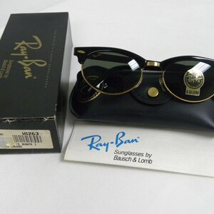 Puede incluir: Gafas de sol Ray-Ban negras con detalles dorados y lentes verdes. Las gafas de sol est&aacute;n en una funda de cuero negra con un bot&oacute;n dorado. La funda est&aacute; sobre una superficie blanca. Las gafas de sol est&aacute;n etiquetadas con "Ray-Ban Sunglasses by Bausch & Lomb".
